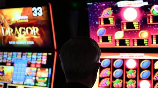 Ein Mann sitzt an einem Spielautomaten und hat vor sich ein Glücksspiel, bei dem man in einer Linie möglichst viele gleiche Symb Merkur-Spielothek