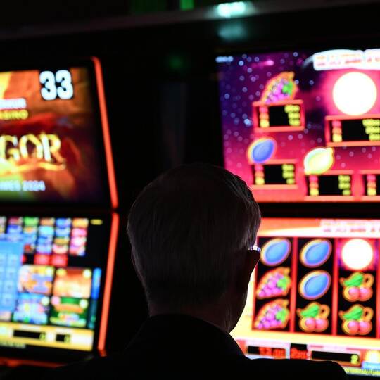 Ein Mann sitzt an einem Spielautomaten und hat vor sich ein Glücksspiel, bei dem man in einer Linie möglichst viele gleiche Symb Merkur-Spielothek